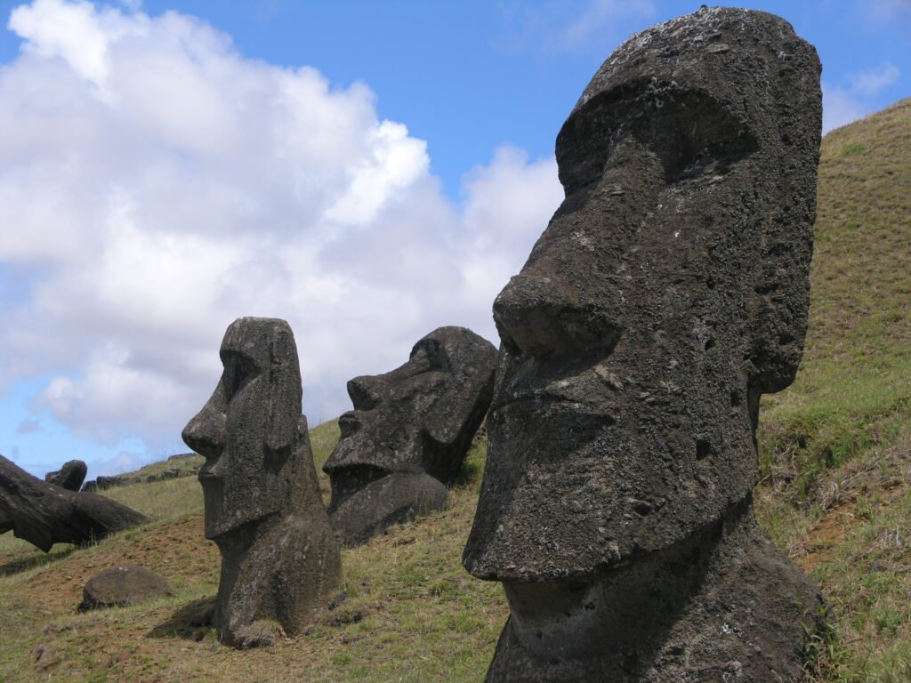 Estatuas moáis de piedra en la ladera de Rano Raraku, Isla de Pascua, bajo un cielo parcialmente nublado.
