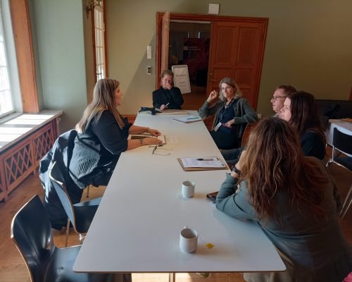 Grupo de personas reunidas alrededor de una mesa blanca participando en una reunión.